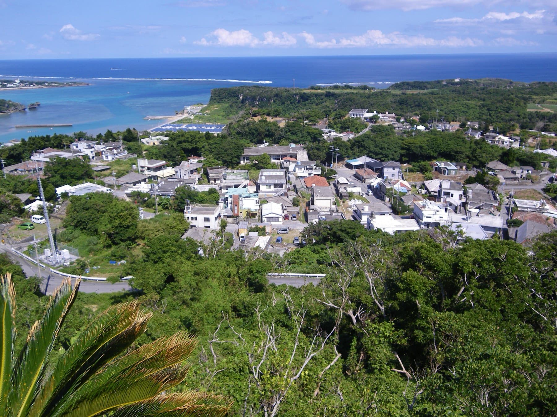 Houses of the Uehara and Miyagi districts spread across a green hilltop on Miyagi, with a sheltered lagoon and the reef line of the open sea beyond