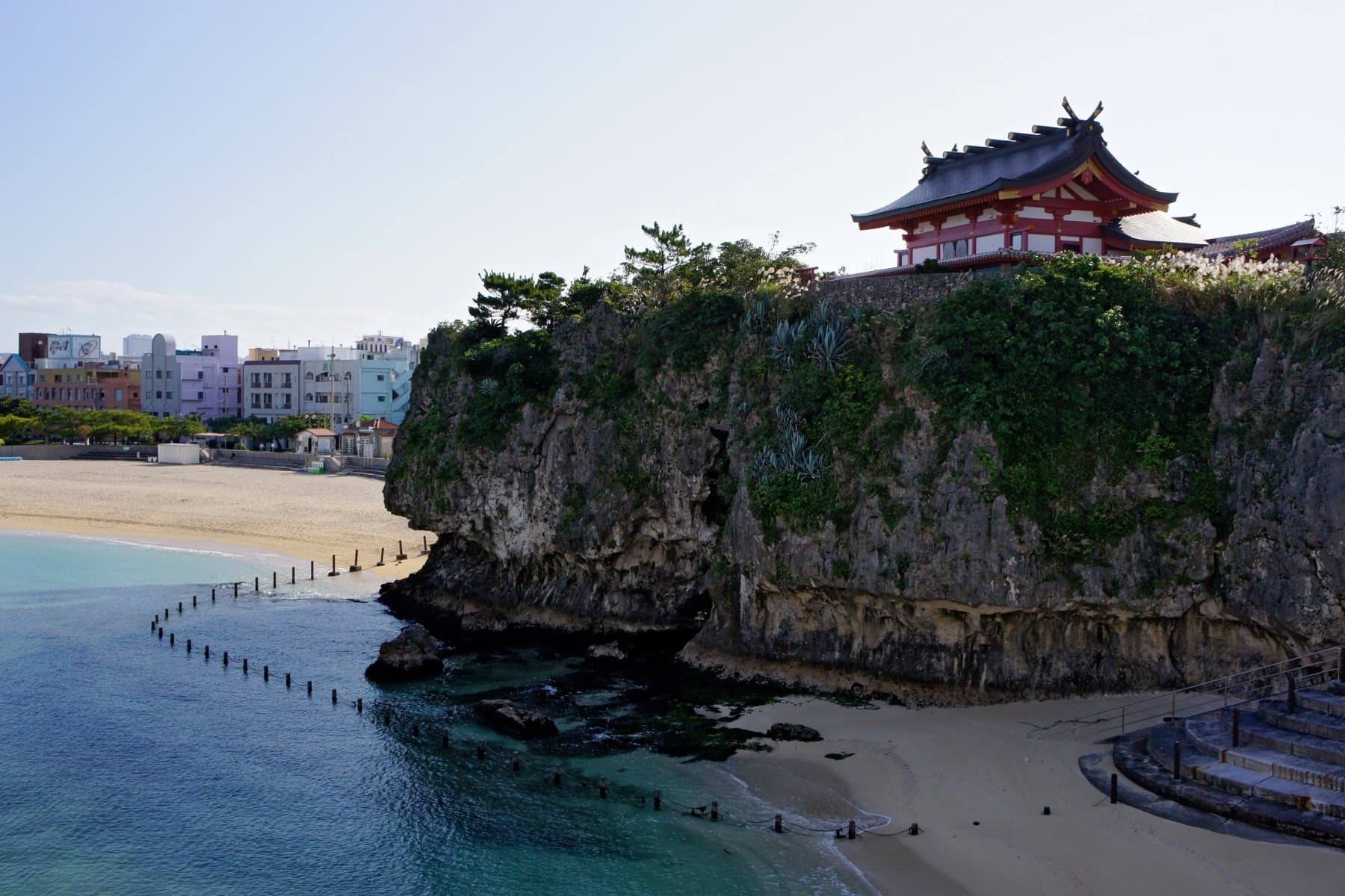 The red roofs of Naminoue Shrine sit on top of a sheer limestone cliff above the small beach and clear green water of Naminoue in Naha.