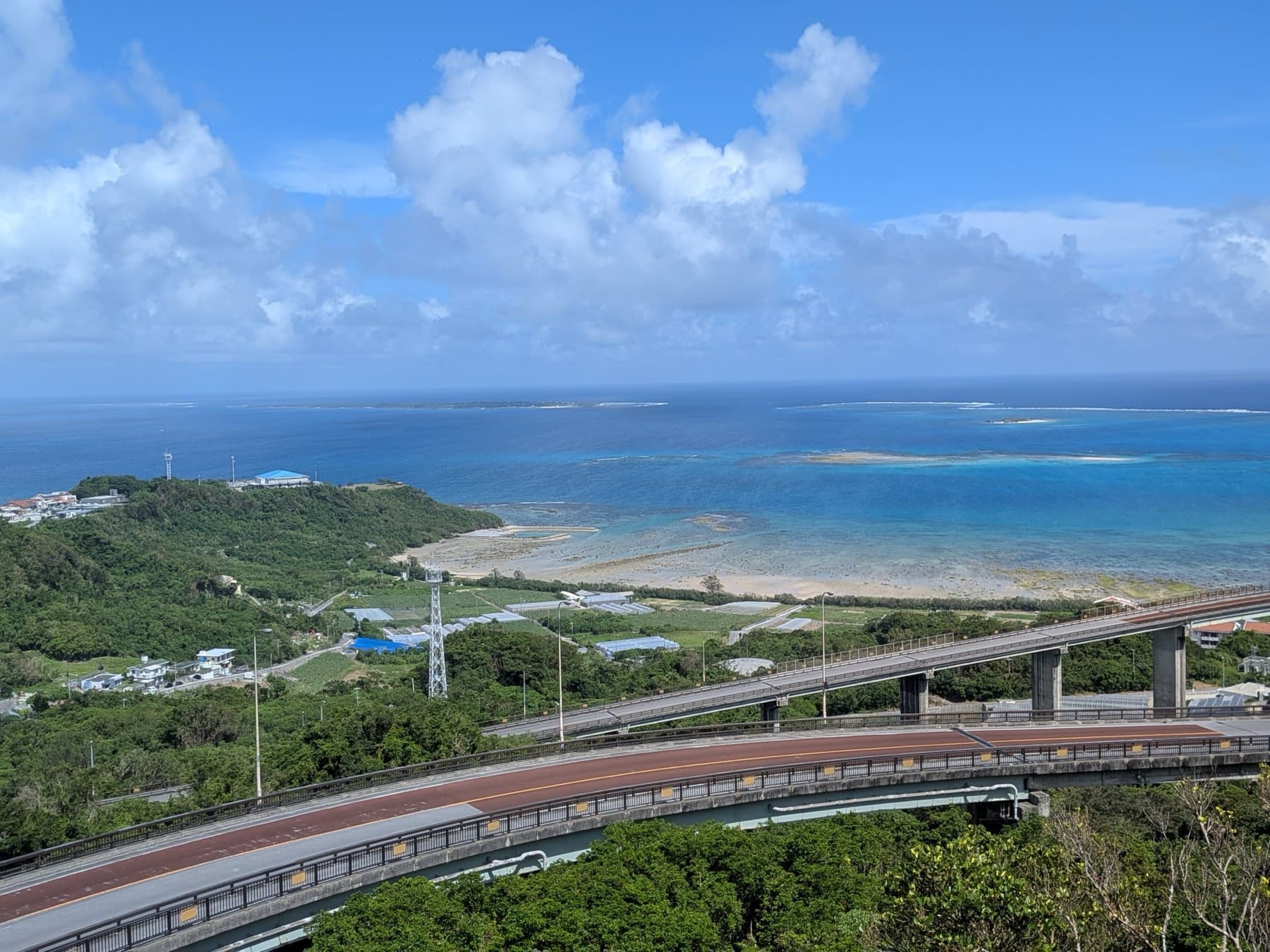 From the top of the Niraikanai Bridge the road curves over the trees toward pale reef flats, and the open sea runs out to a line of tall cloud