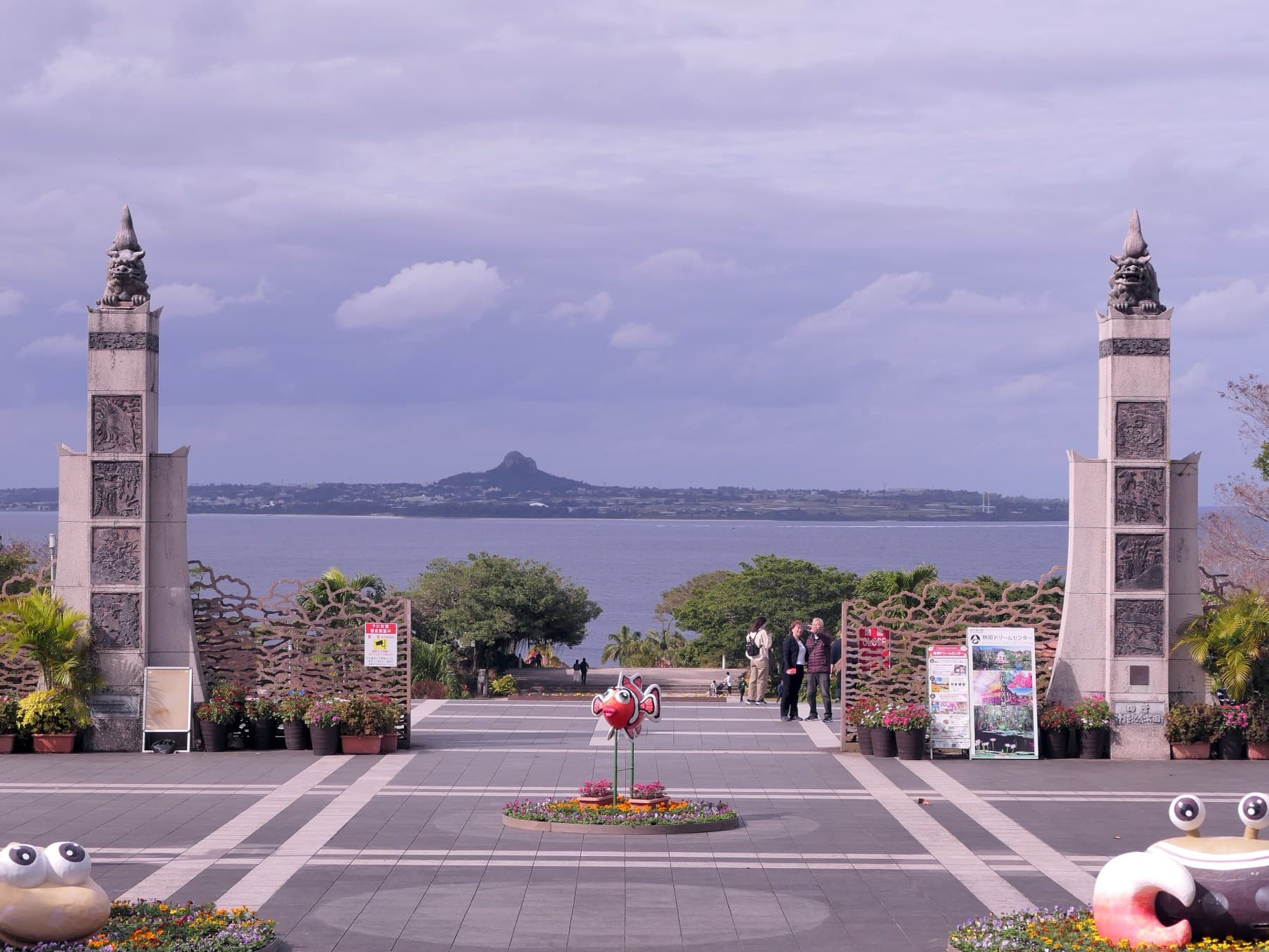 Two carved stone pillars topped with shisa frame the seaward plaza of Ocean Expo Park, and Ie-jima's peak rises across the water between them
