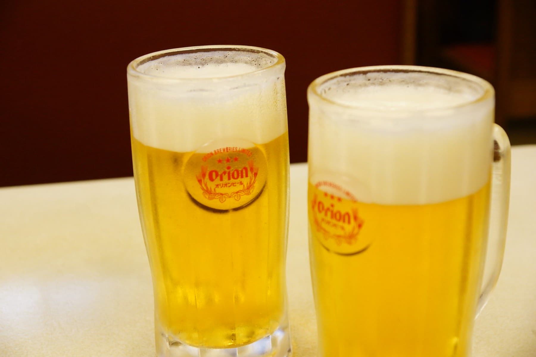 Two frosted mugs of Orion draft beer with thick white heads stand on a pale table at Jack's Steak House in Naha