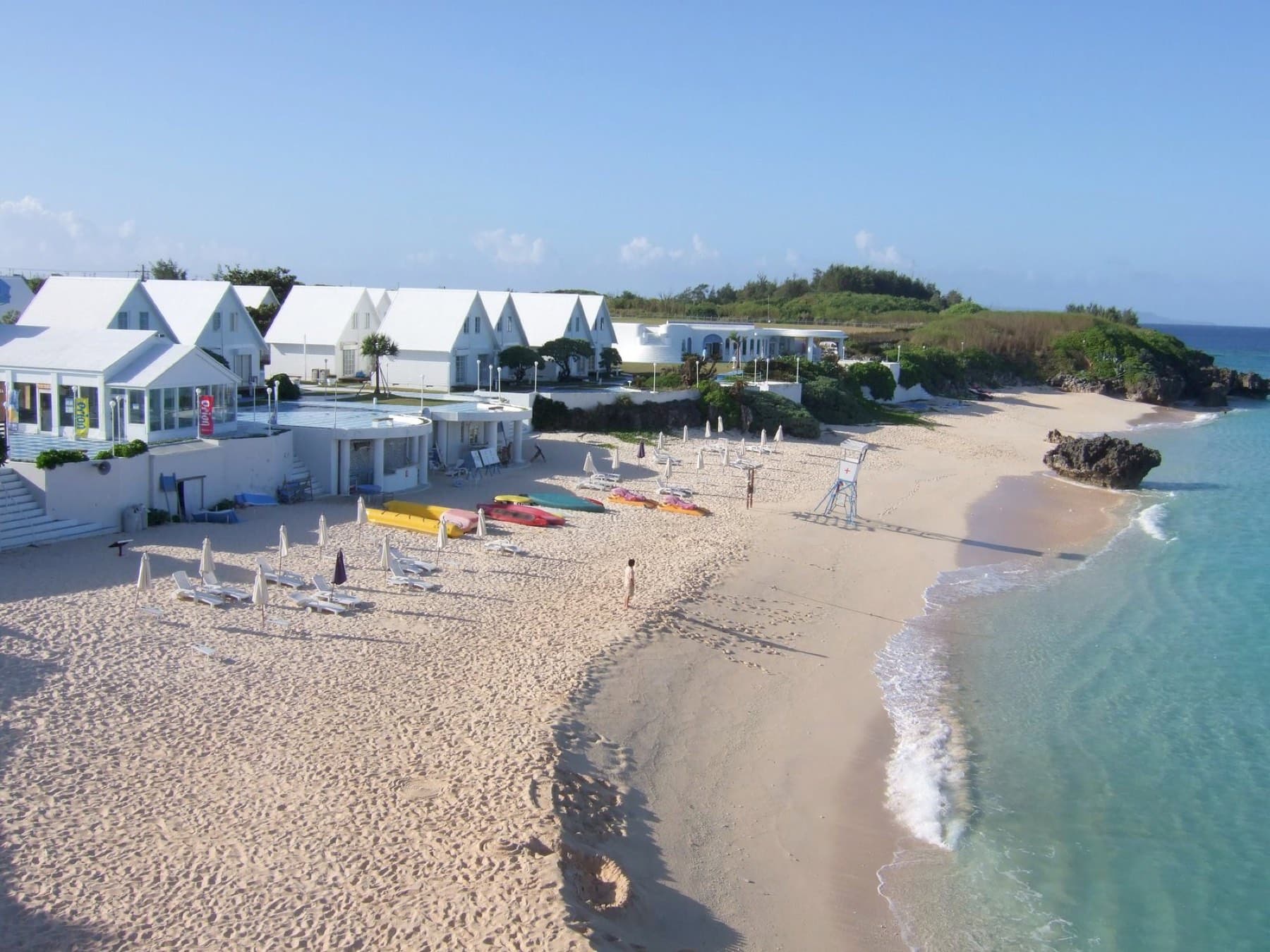 White cottages of Pricia Resort line a curving beach of pale sand where kayaks and loungers wait beside clear water.