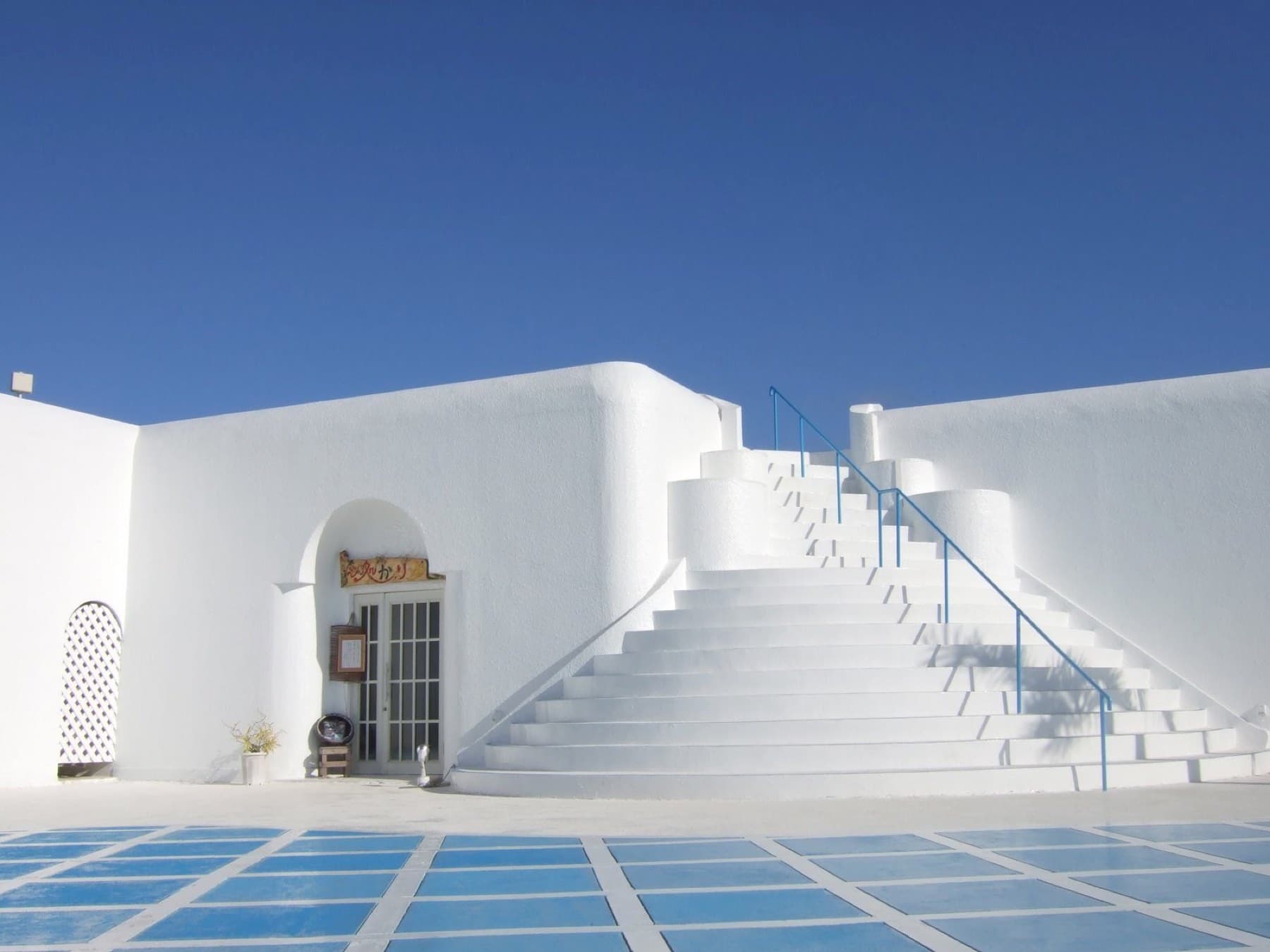 A wide flight of white stairs climbs between whitewashed walls at Pricia Resort on Yoron under a cloudless sky.