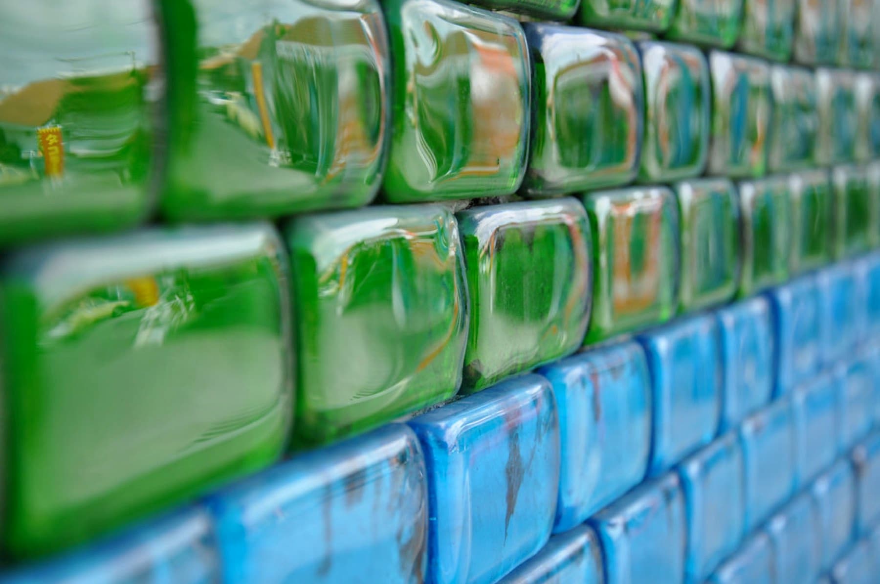 A wall built from green and blue recycled glass blocks catches the light at Ryukyu Glass Village, with the rows fading out of focus