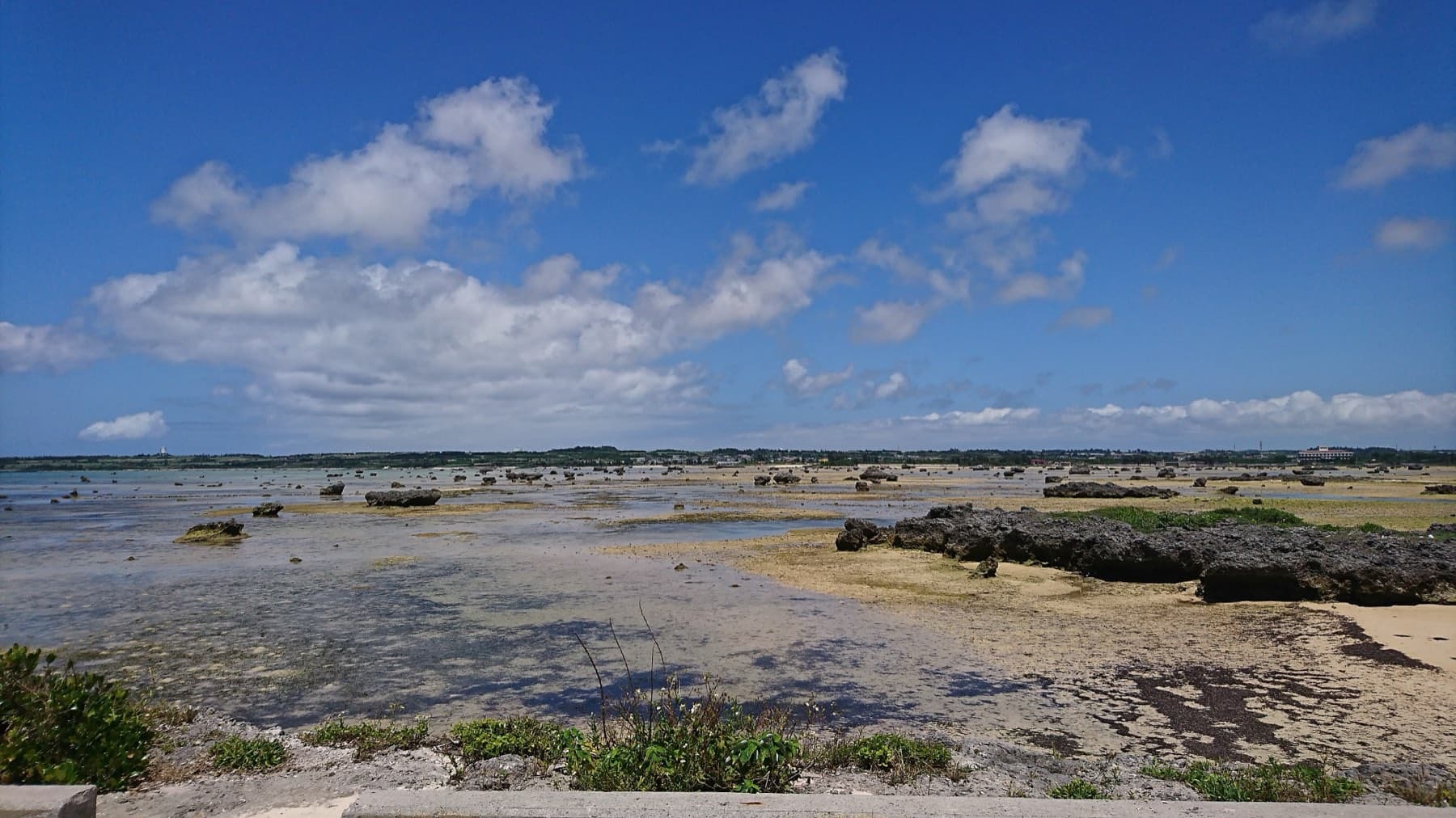 Big coral boulders lie scattered across the wide, flat reef of Sawada no Hama on Irabu under a bright sky of small clouds.