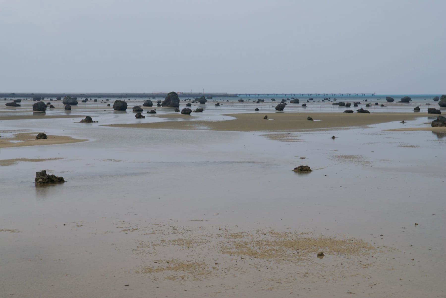 At low tide the shallow flats of Sawada no Hama stretch out toward rows of tumbled boulders under a grey sky.
