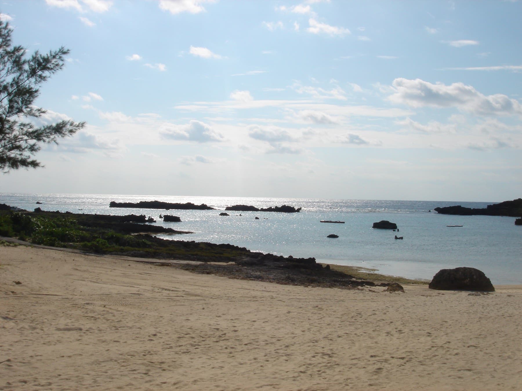 Dark coral rocks break the calm water off the grey sand of Shigira Beach on a hazy late-autumn afternoon.