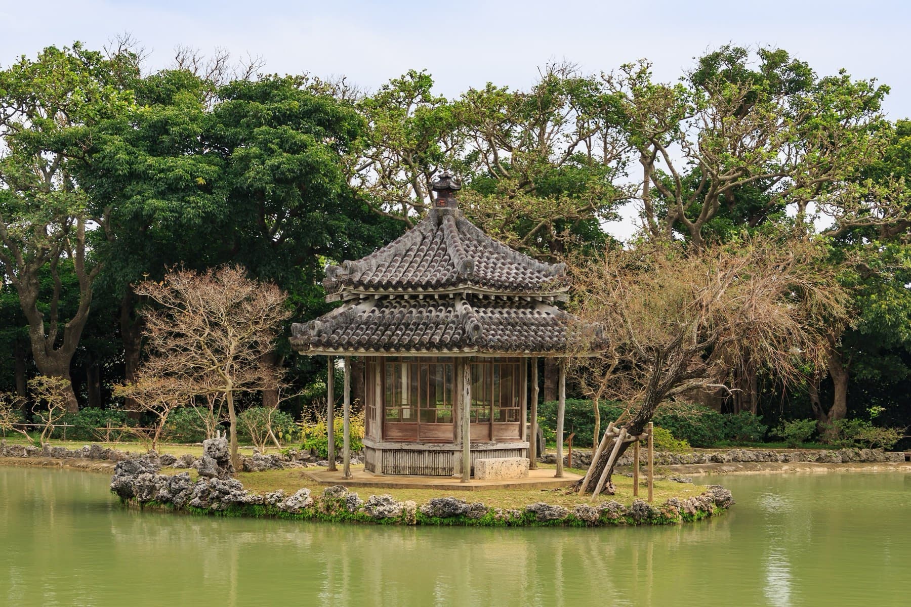 The hexagonal Rokkakudo pavilion with its grey tile roof sits on a tiny island in the green pond of the Shikinaen royal garden in Naha