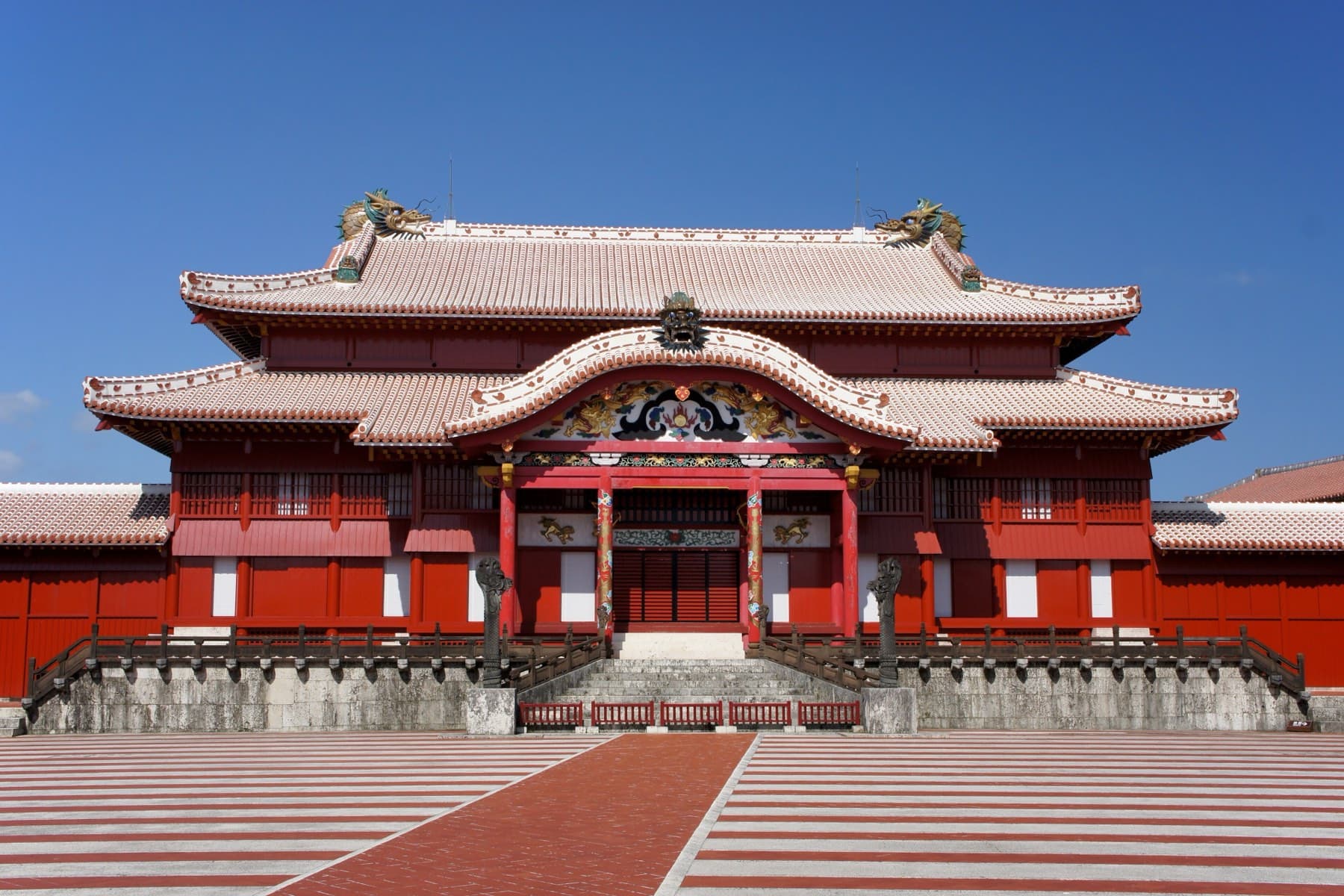 The red lacquered Seiden of Shuri Castle faces a courtyard striped in pale and red tiles under a deep blue sky
