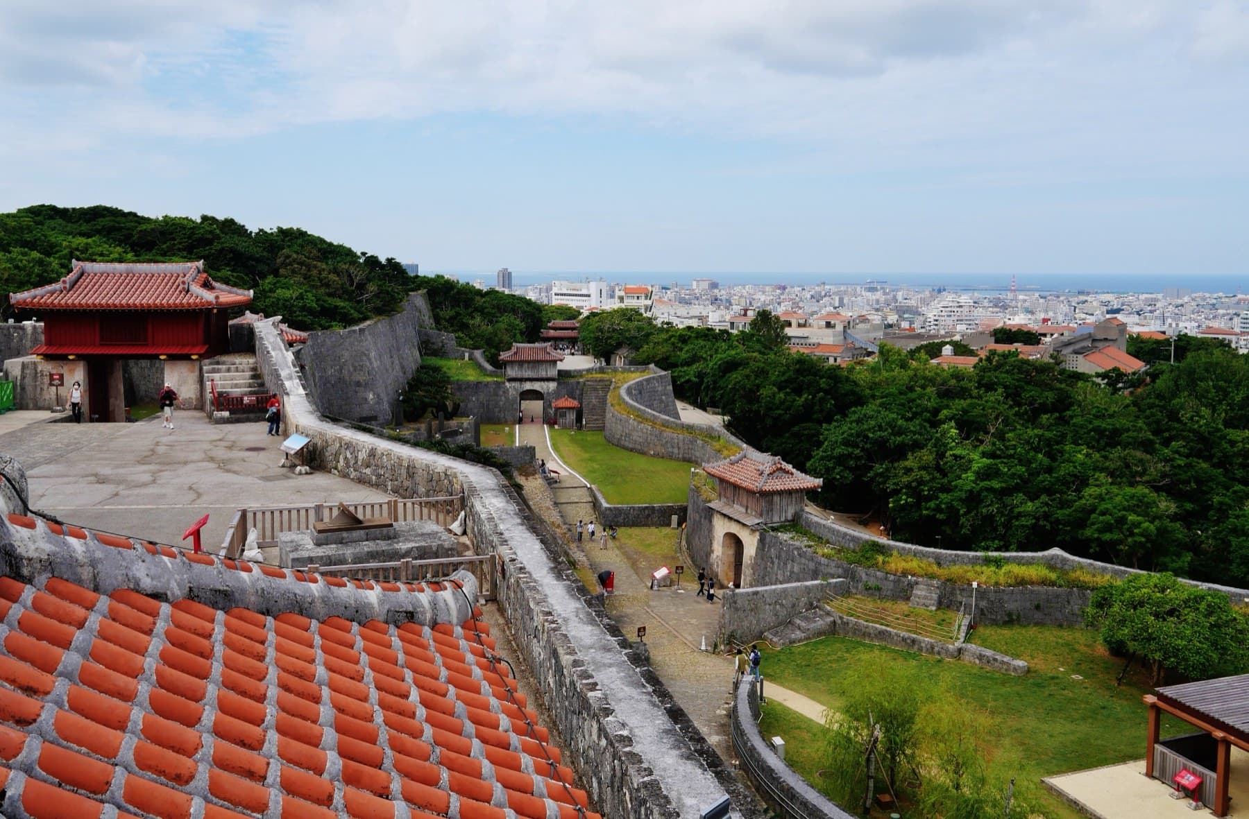 From high on Shuri Castle the curving limestone walls and gatehouses step down the hill toward the rooftops of Naha and the sea
