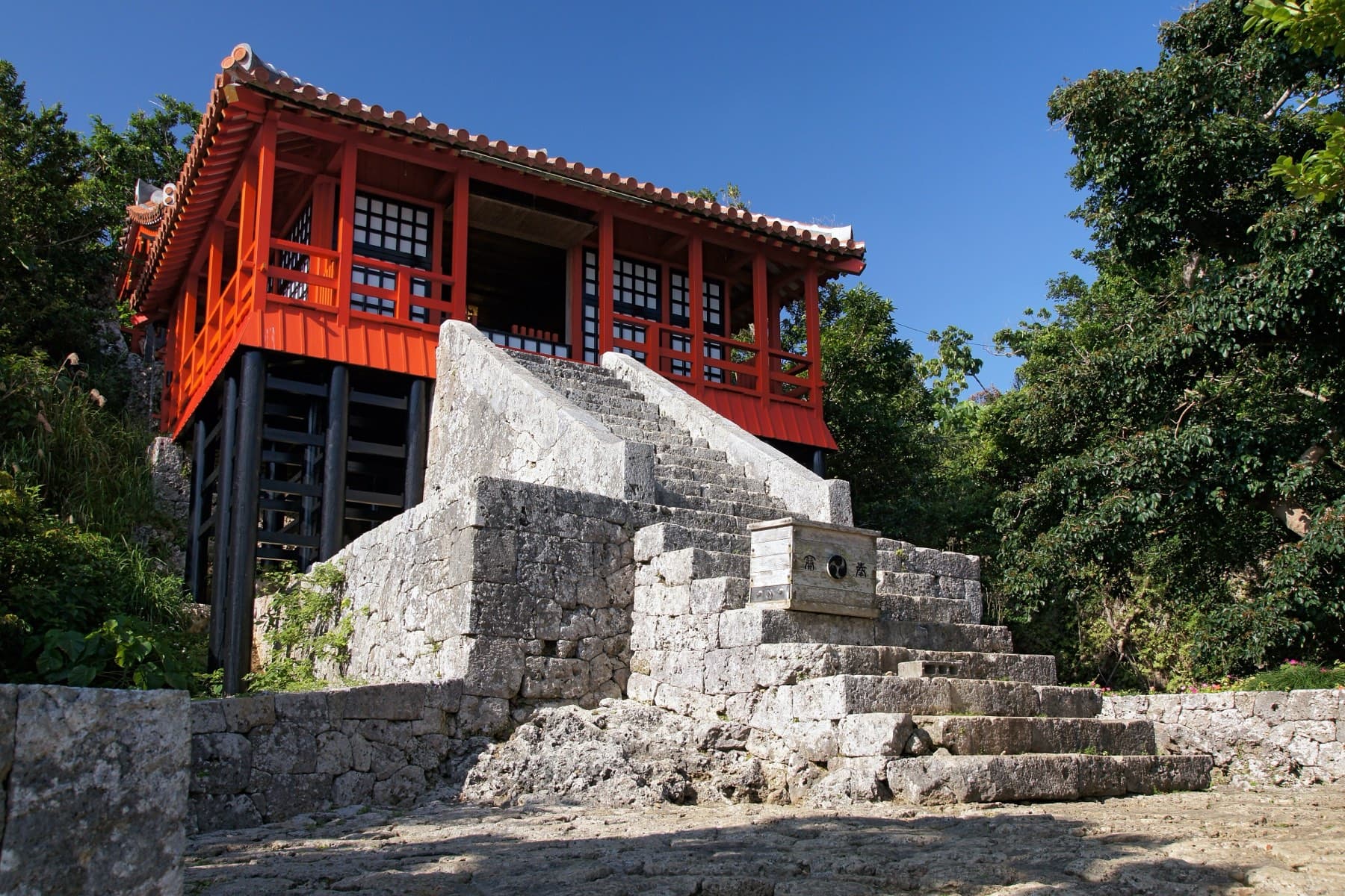 The red lacquered hall of Sueyoshi Shrine stands on a high limestone platform reached by worn stone steps in the woods of Sueyoshi Park