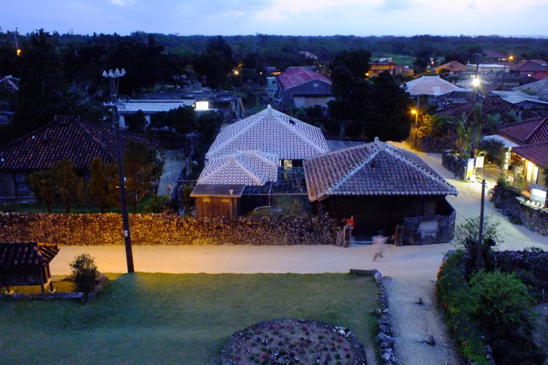 Street lamps come on along the sand lanes of Taketomi village at dusk as the last light fades over the tiled roofs.