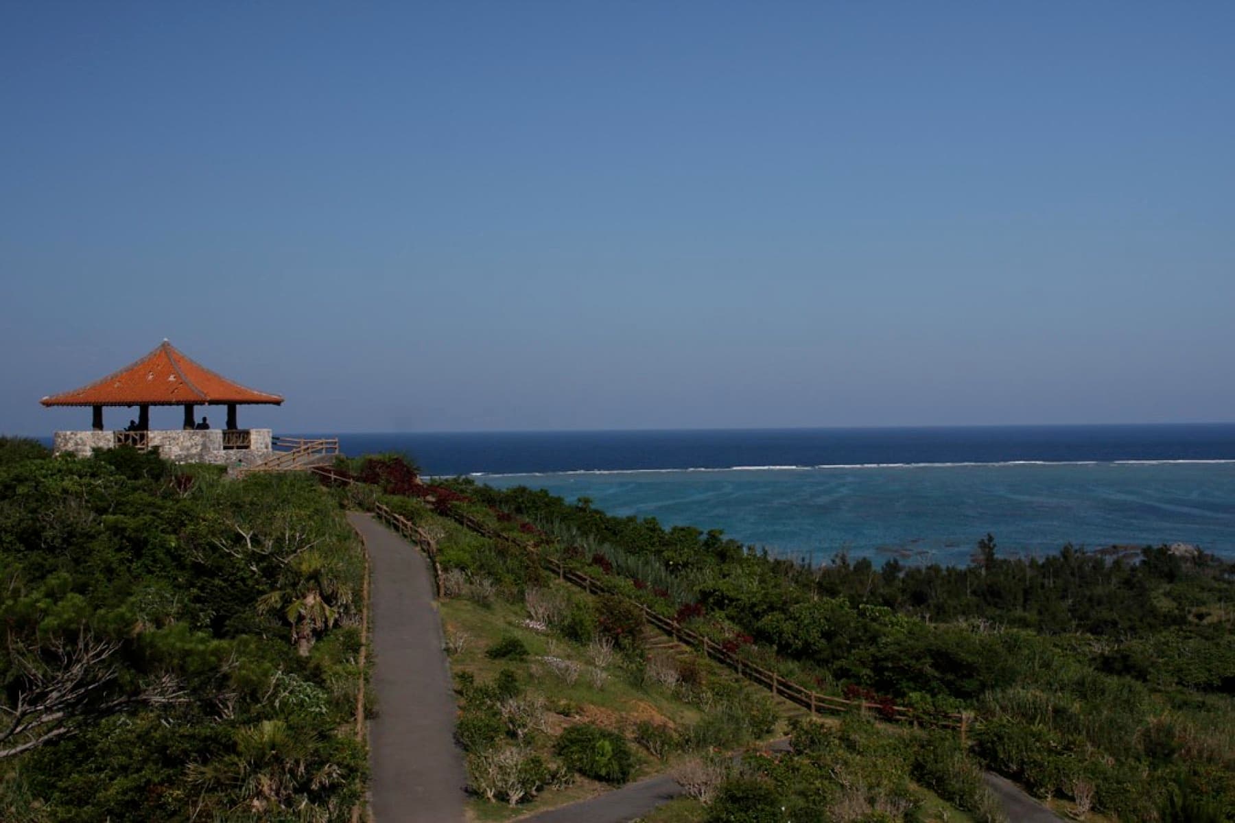 A paved path climbs through low scrub to the red-tiled pavilion at Tamatorizaki, where the reef edge draws a white line across the deep blue sea.