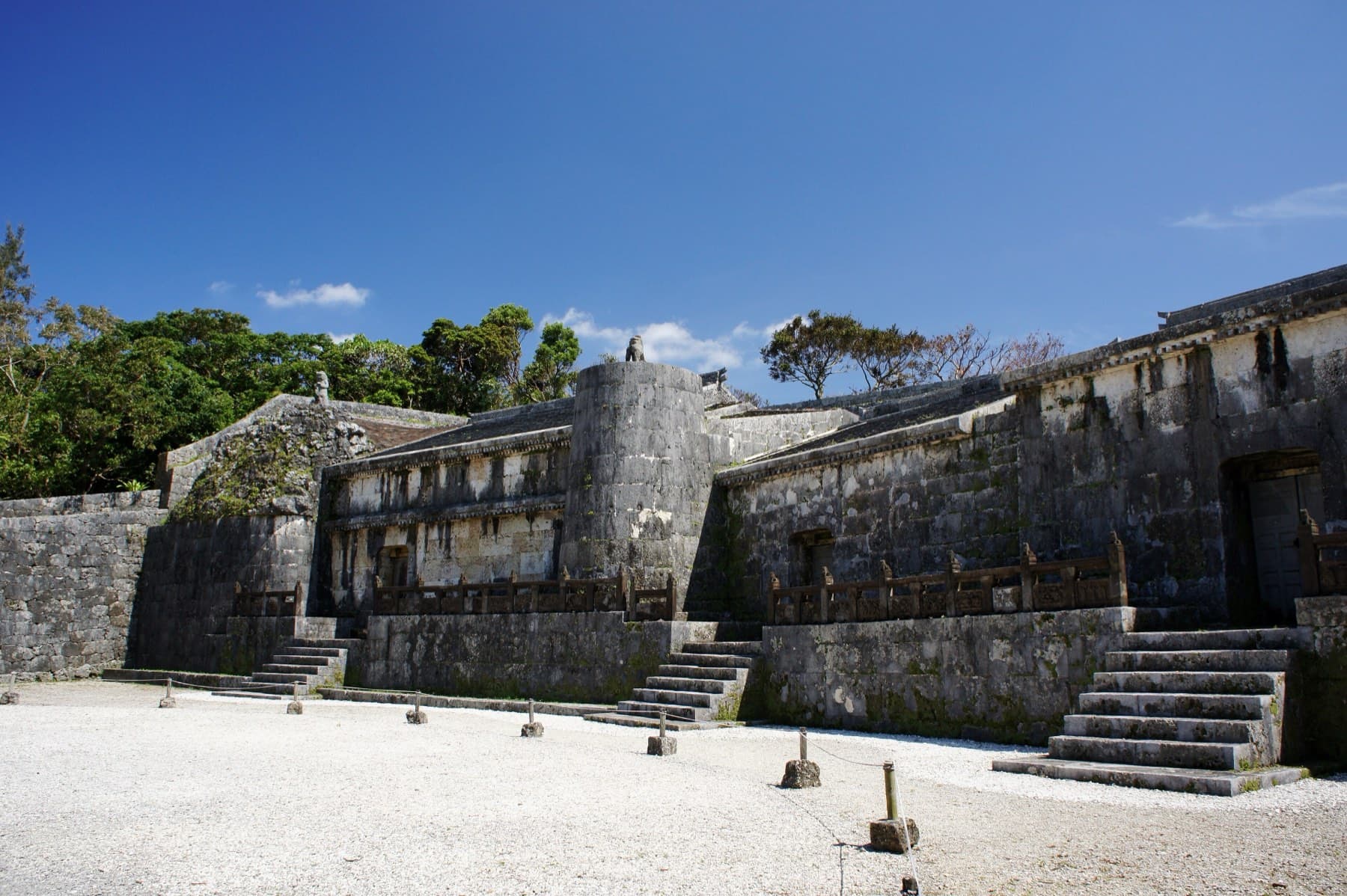 Three stone burial chambers of the Tamaudun royal mausoleum line a raked courtyard of white coral gravel under a clear blue sky in Shuri
