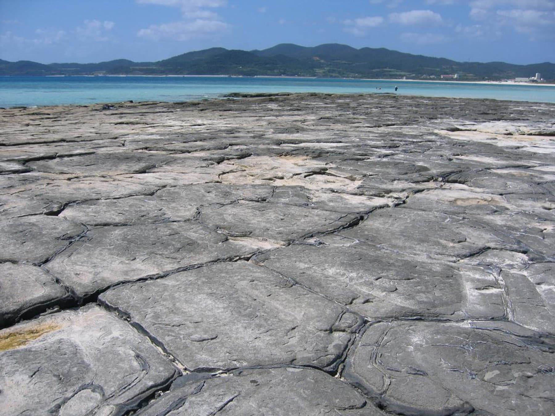 Pentagonal and hexagonal slabs of lava rock form the flat pavement of Tatami-ishi on Ou-jima, with the low hills of Kume-jima across the water