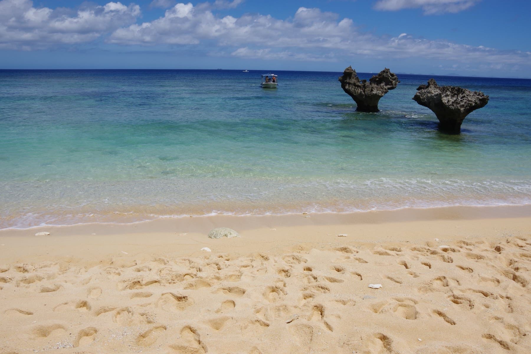 Footprints cover the pale sand of Tinu Beach on Kouri as small waves roll in toward the two rocks of Heart Rock standing offshore