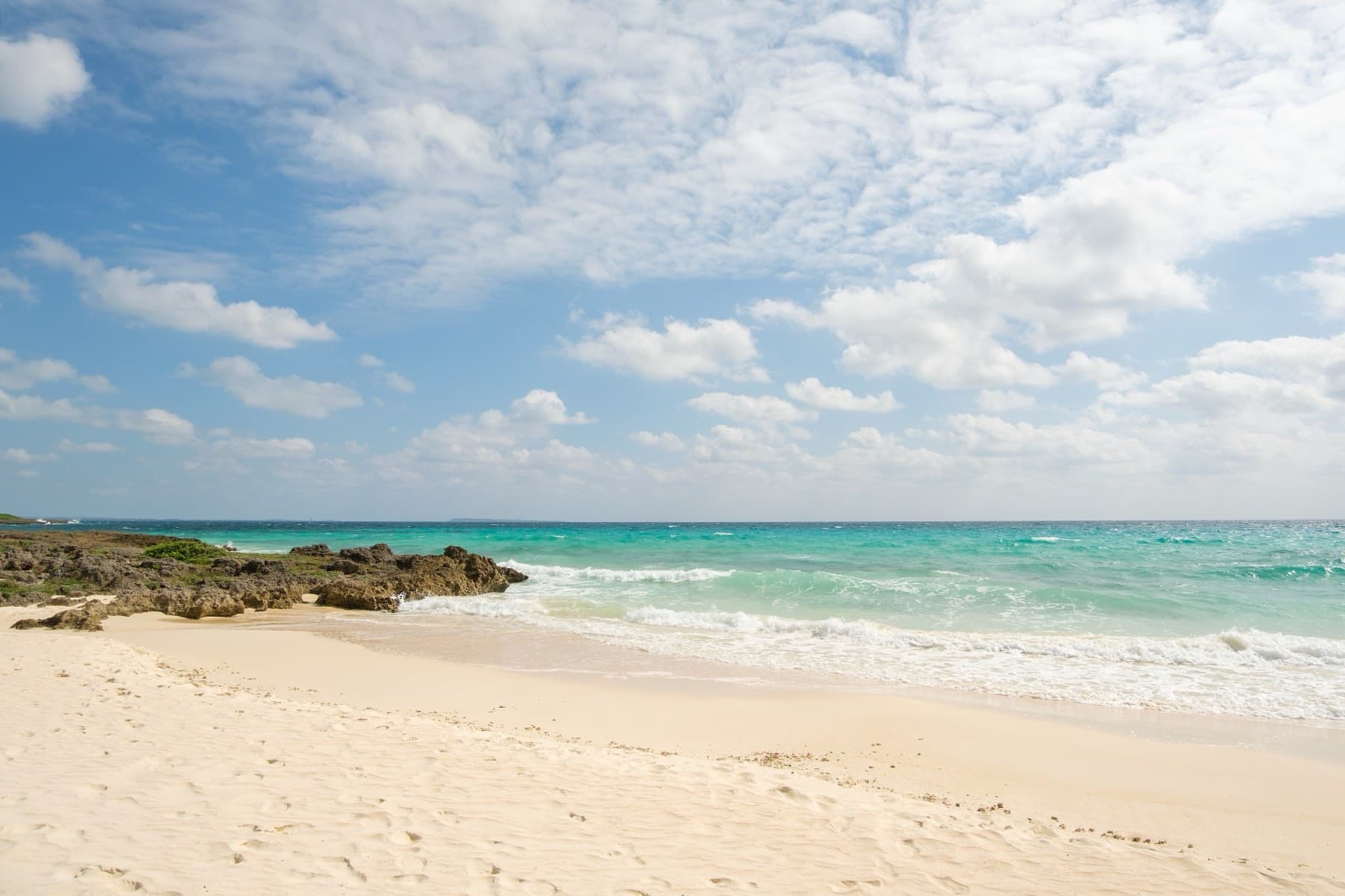 Low waves fold onto the soft white sand of Toguchi no Hama as the sea shades from aqua to deep blue under winter cloud.