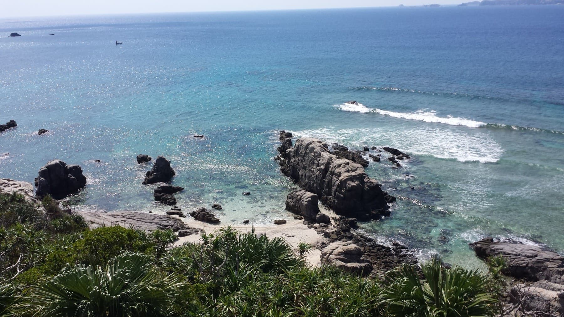 From the Aharen lookout, rocky headlands and scrub fall to a shallow reef where waves break white on clear blue water along the south coast of Tokashiki.