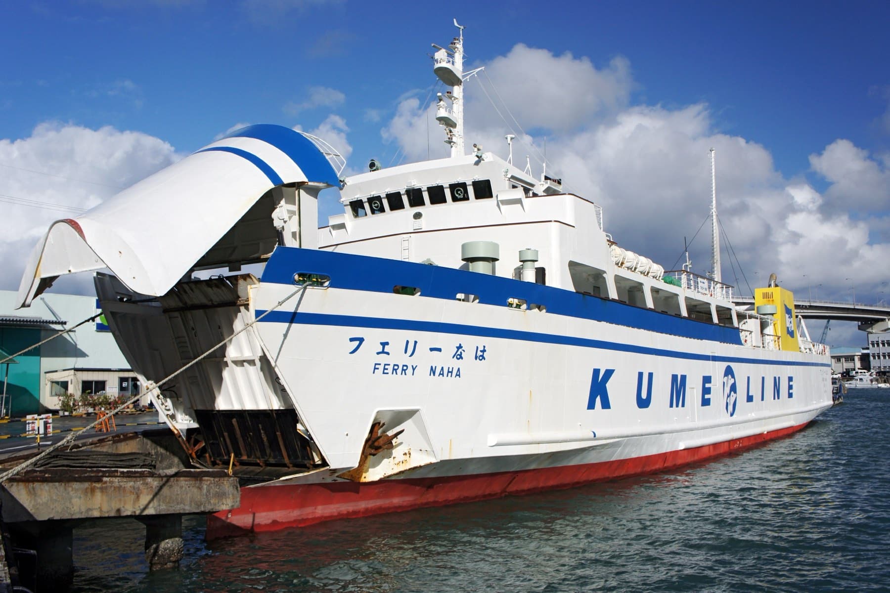 The white and blue Kume Line car ferry Ferry Naha lies moored at Tomari Port with its bow ramp raised under a blue sky