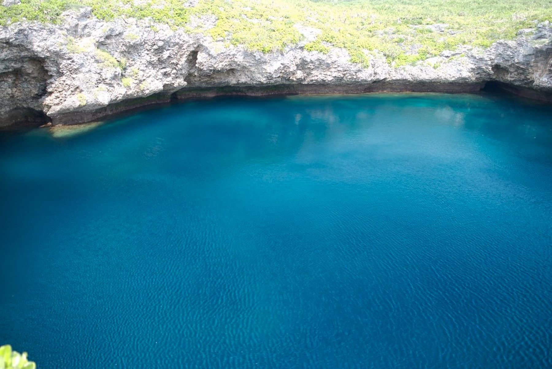 Deep blue water fills the round basin of Toriike below a ledge of eroded limestone on the west coast of Shimoji.