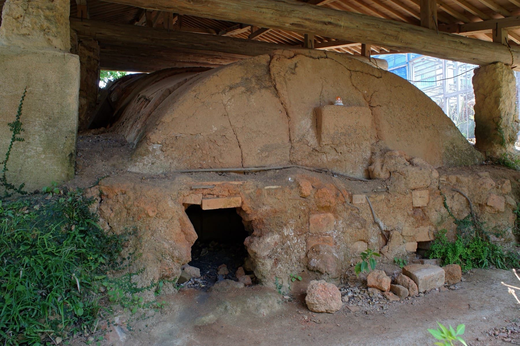 An old climbing kiln built of red clay and brick rests under a timber shelter in Tsuboya, and its small stoking mouth opens at the front