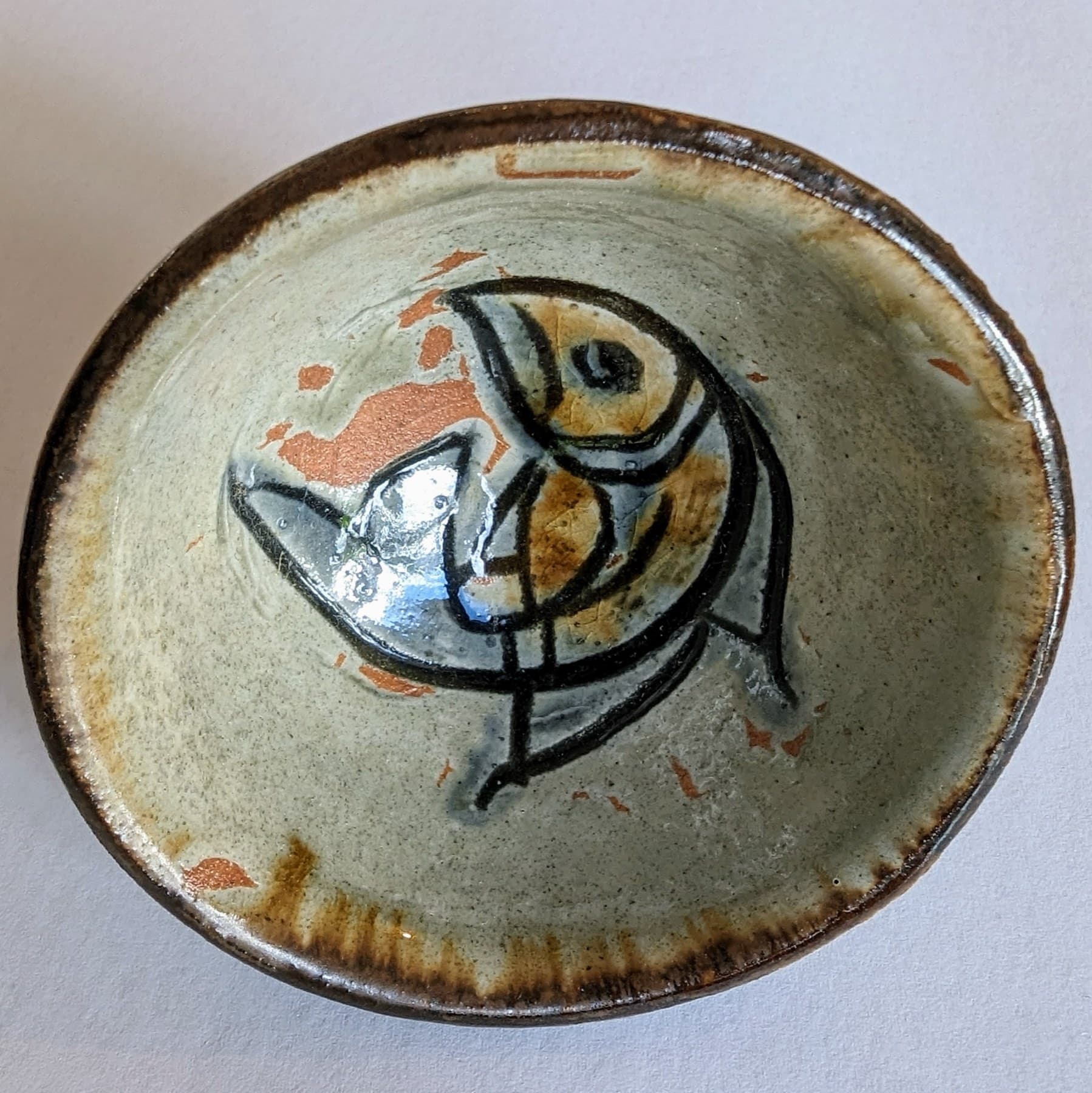 A small stoneware plate by the Okinawan potter Jiro Kinjo carries his fish motif in black and blue brushwork over a pale grey glaze