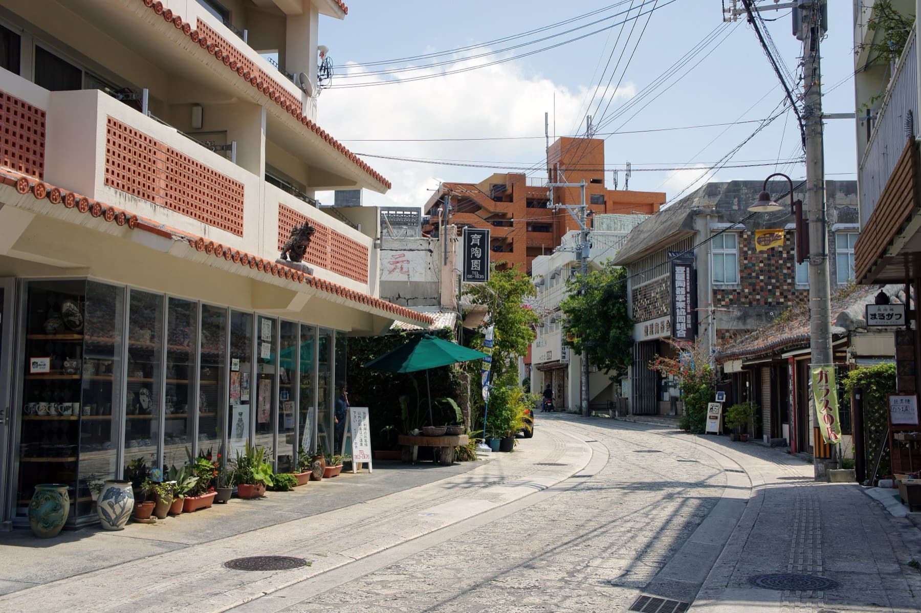 Pottery shops with red tile roofs and potted plants line the stone-paved Tsuboya Yachimun Street as it curves gently uphill on a sunny afternoon