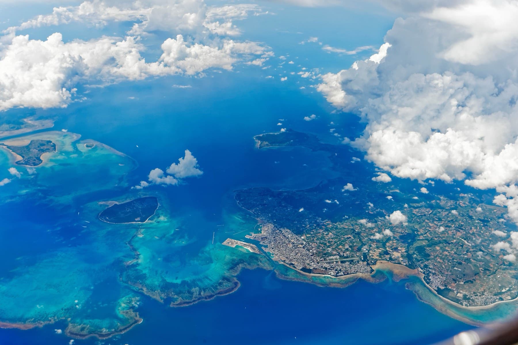 From the air the western half of Ishigaki and its town give way to wide reefs and the flat islands of Taketomi and Kohama under scattered cloud.