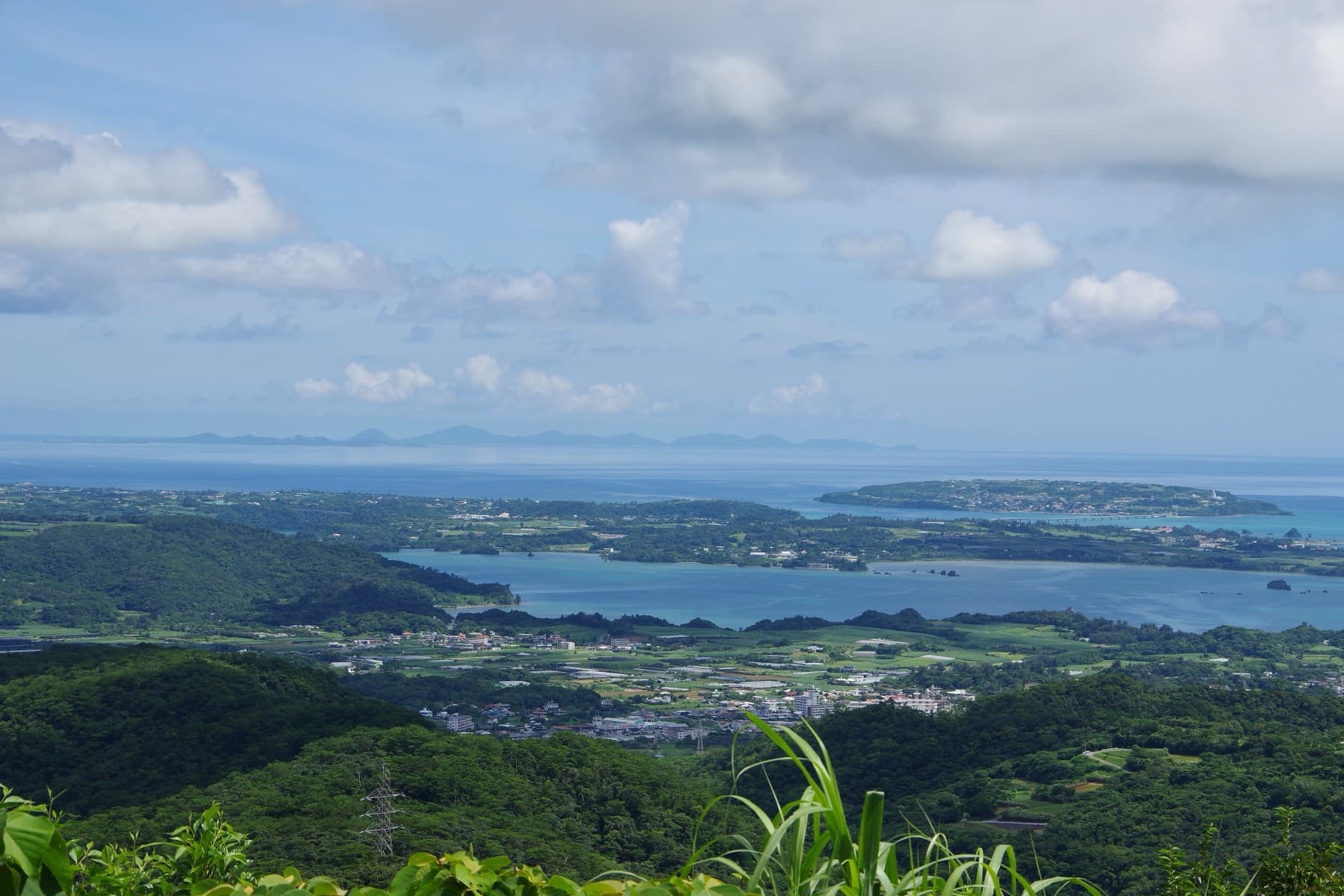 Seen from Mount Nago, the Haneji inlet wraps around low Yagaji, and Kouri lies beyond it with the outer islands faint on the horizon