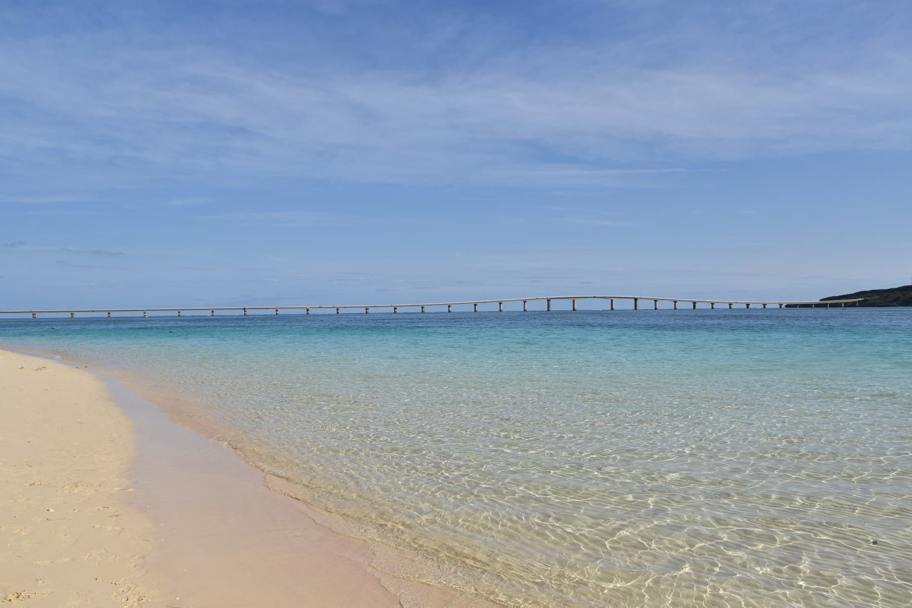 Sand ripples show through glassy shallow water at Yonaha Maehama, and the Kurima Bridge draws a thin line across the bay to Kurima.