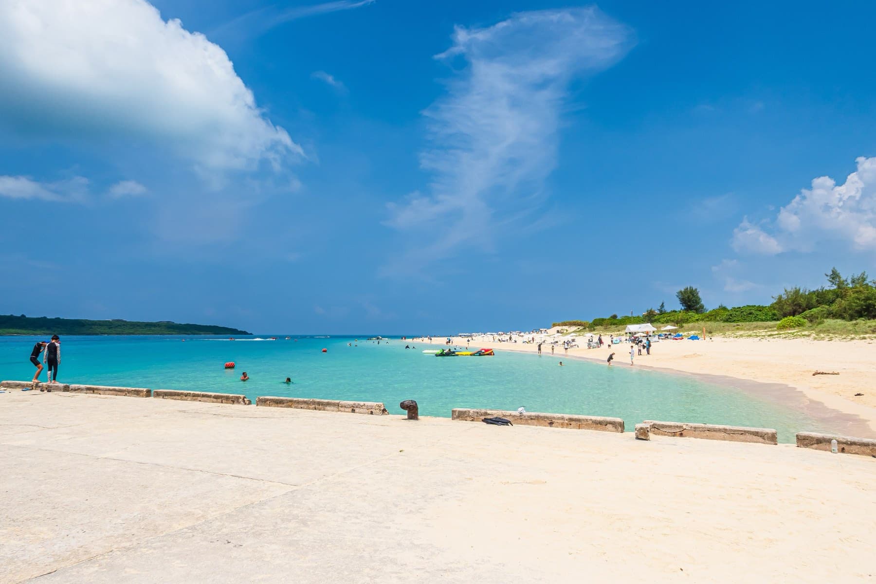 Summer visitors spread along the white sand and bright blue water of Yonaha Maehama on a clear late morning.