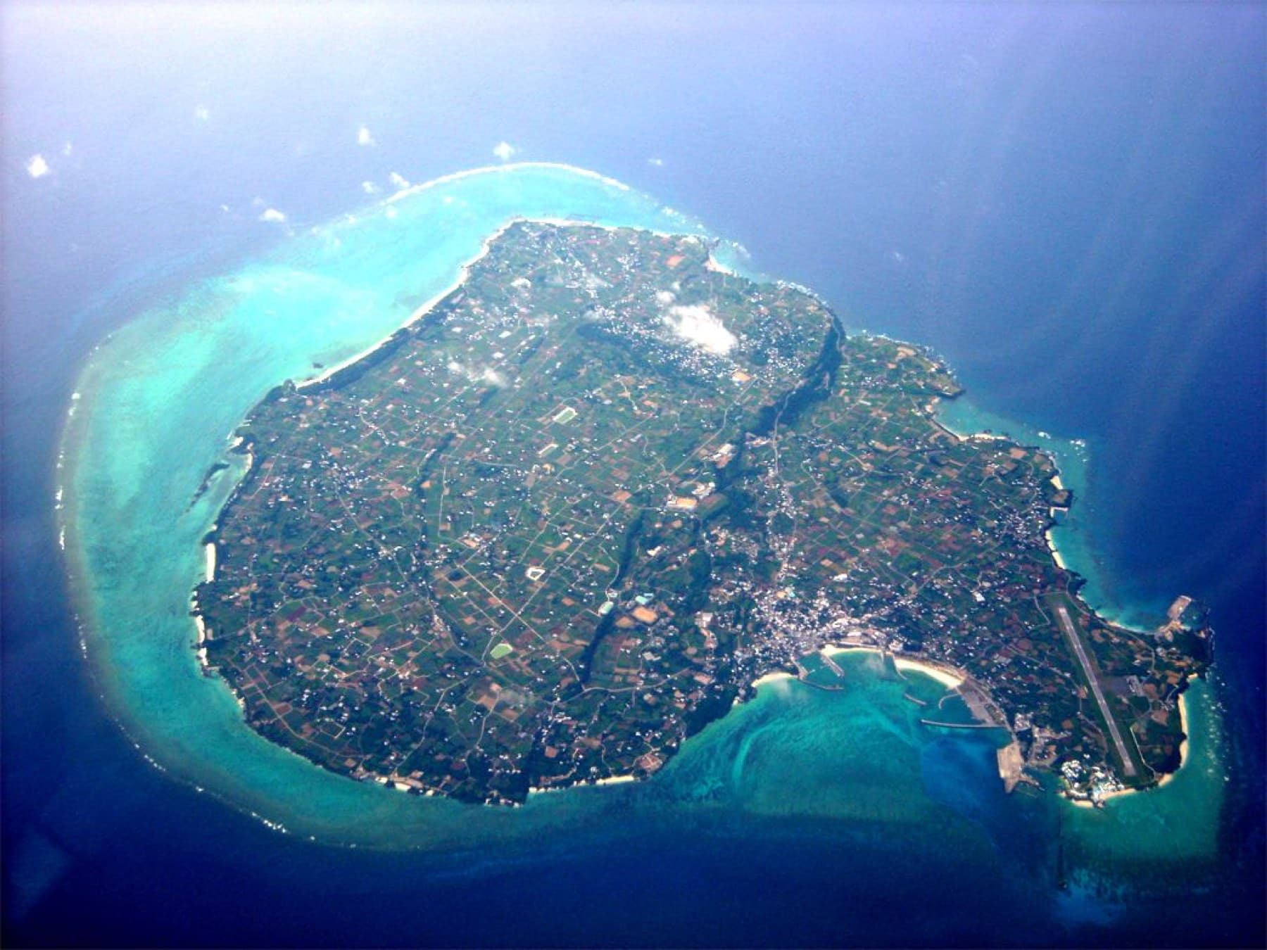 Seen from high above, Yoron lies as a small green island wrapped in a wide pale reef in the deep blue sea.